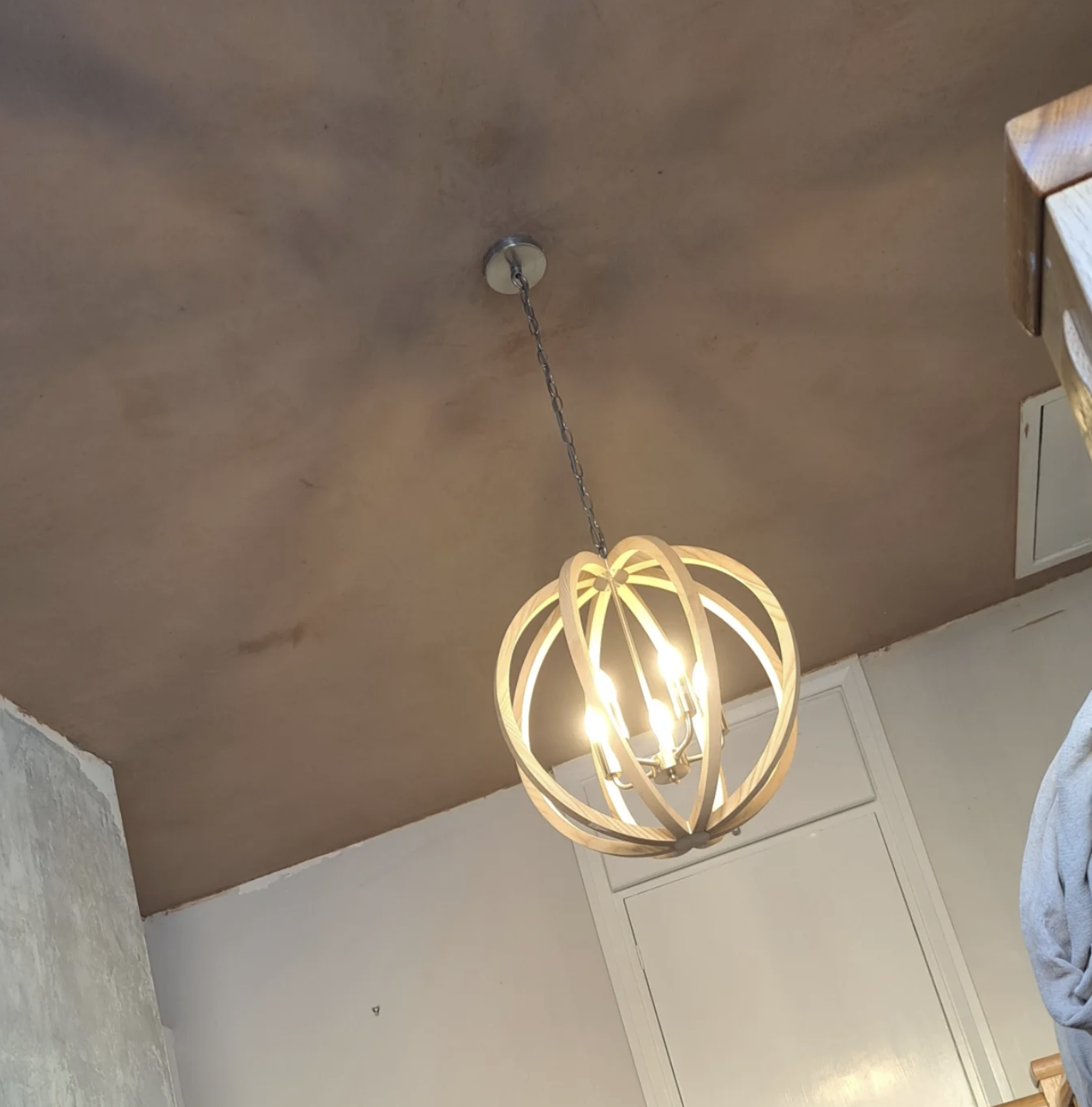 Modern pendant chandelier with wooden or metal rings surrounding multiple light bulbs hanging from a chain on a textured ceiling.
