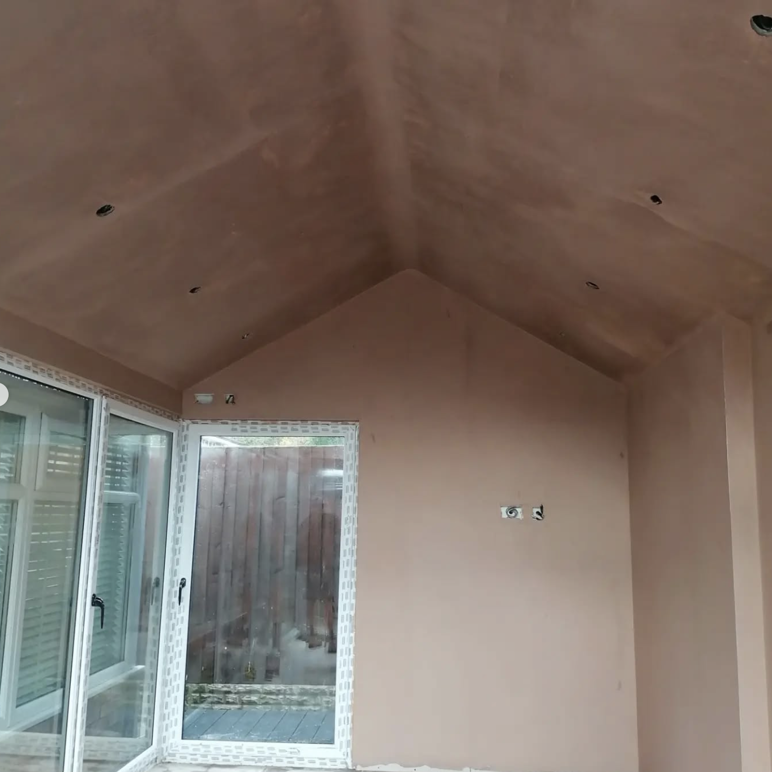 Interior of a room under construction with an angled ceiling, electrical wiring, and a sliding glass door leading outside.