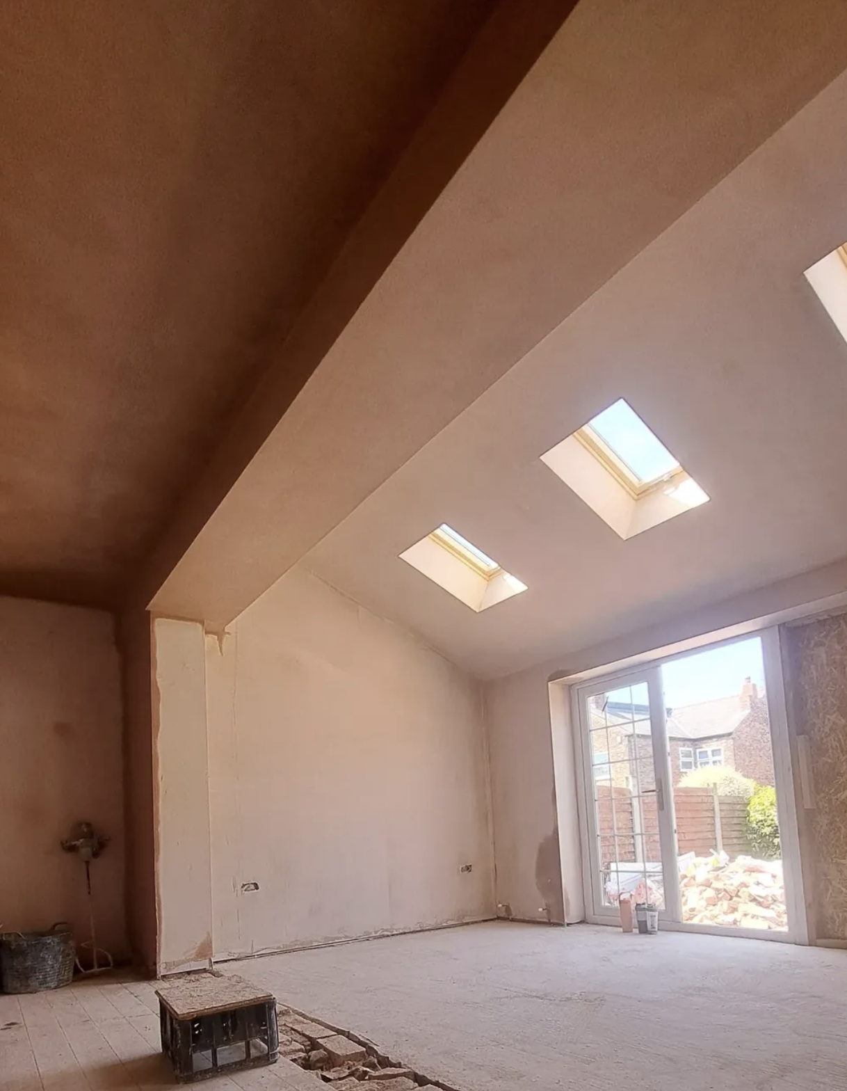 Room under construction with unfinished walls, a wooden floor, and three skylights on the ceiling, with a glass door leading to an outdoor area.