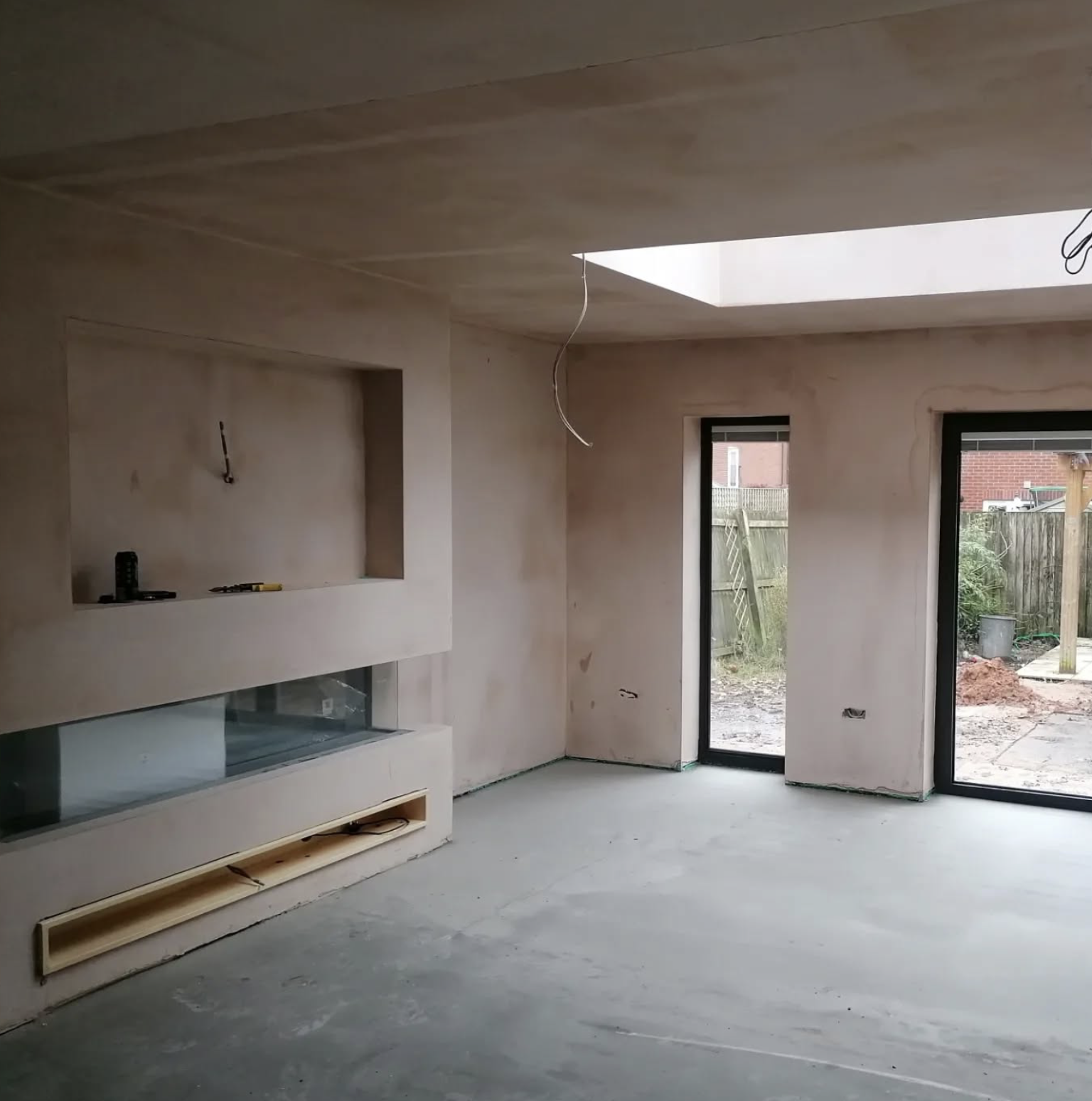 Interior of a room under construction with unfinished drywall, large glass sliding doors, and a skylight in the ceiling.