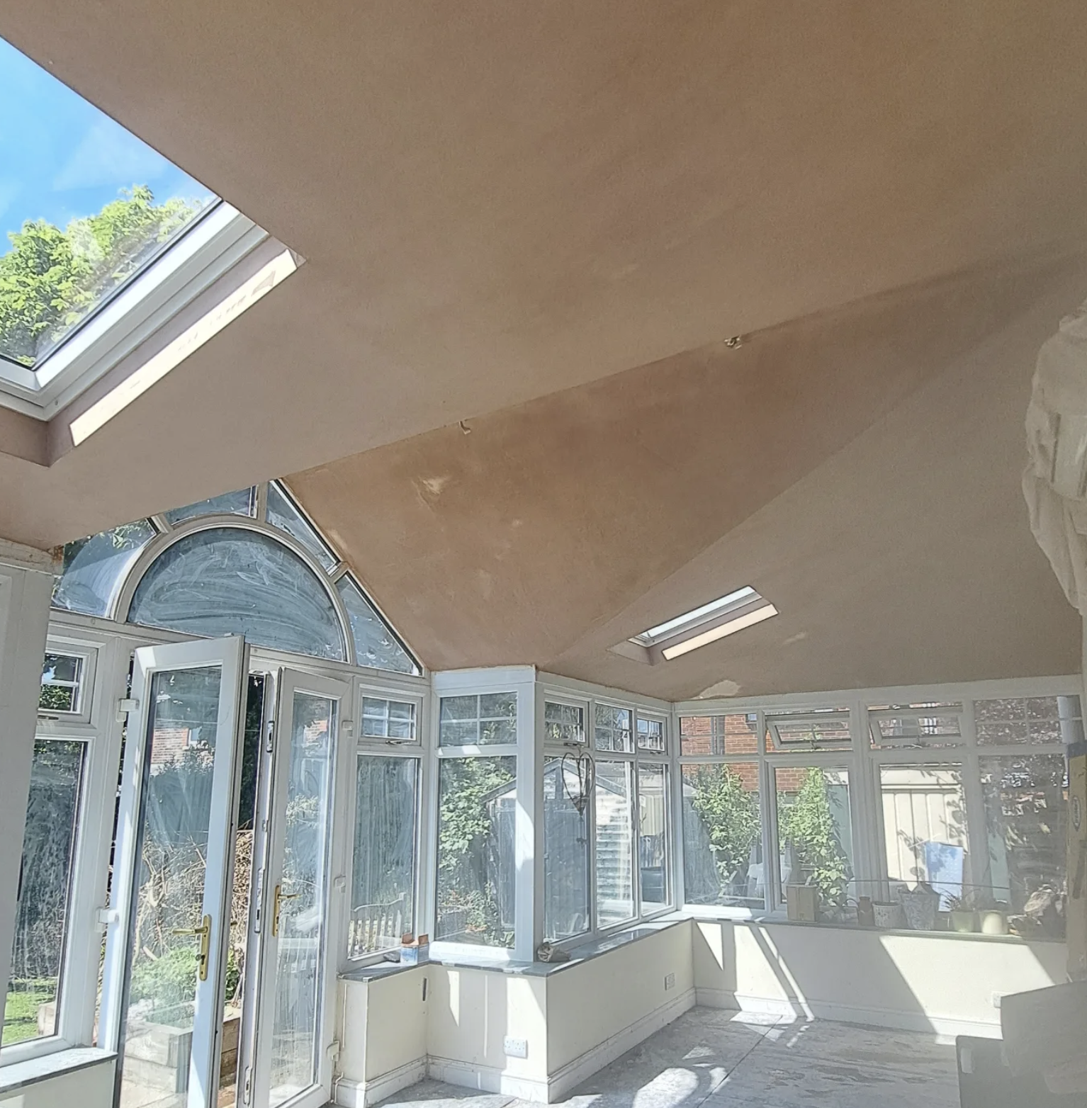 Bright conservatory with large windows, skylights, and a view of a garden outside.