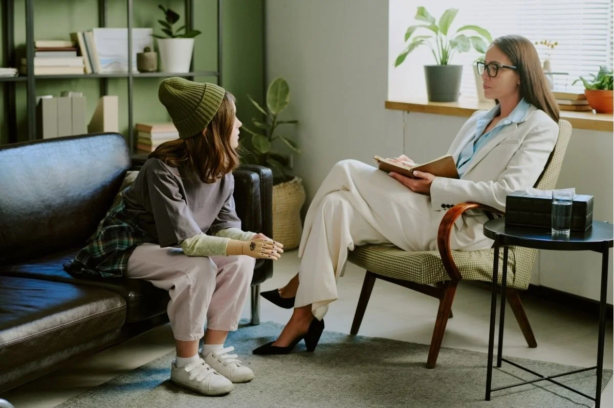 Female psychologist speaking with child seated on couch during child therapy session in cozy office.