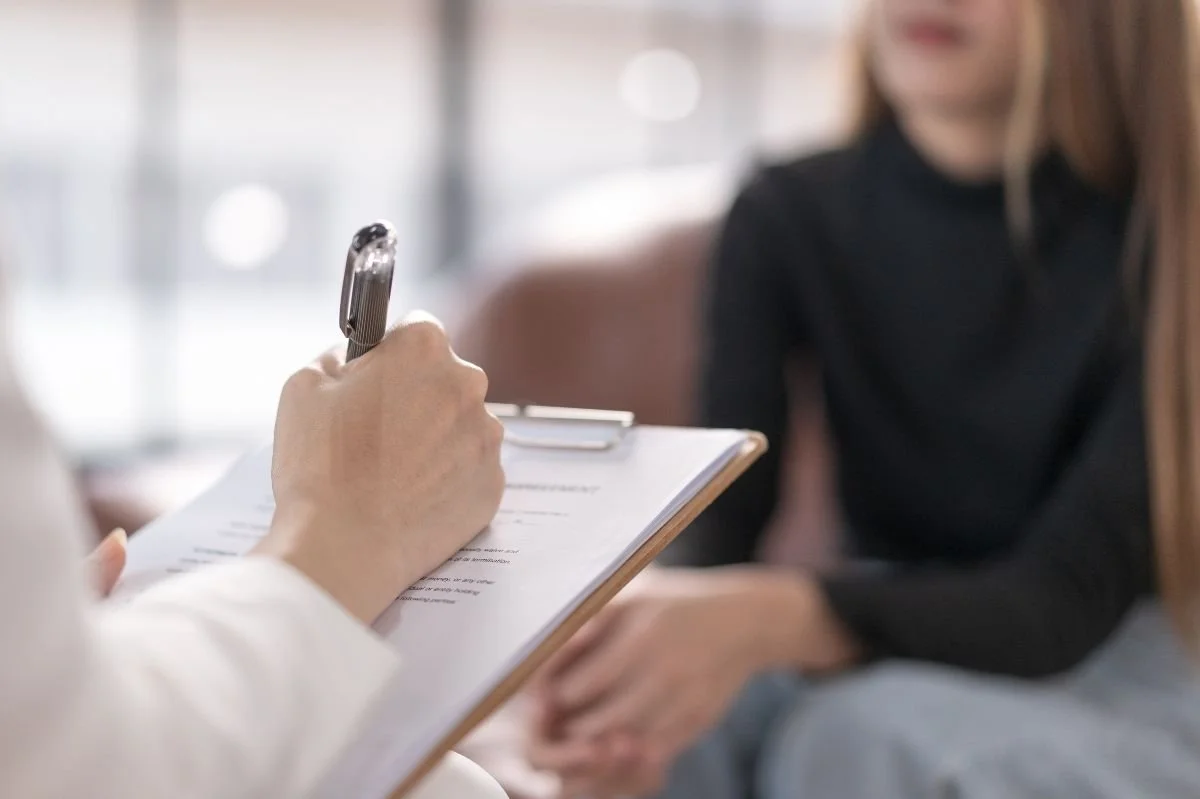 Close up of therapist writing notes on clipboard while client sits in background.