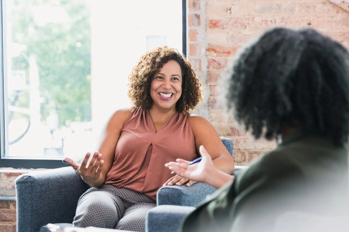 Woman smiling and speaking with therapist while seated in a comfortable counseling office.
