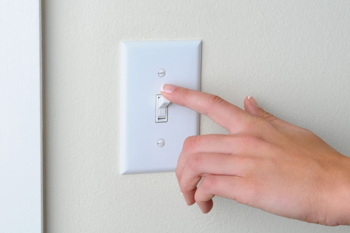 Close up of hand turning on a wall light switch.