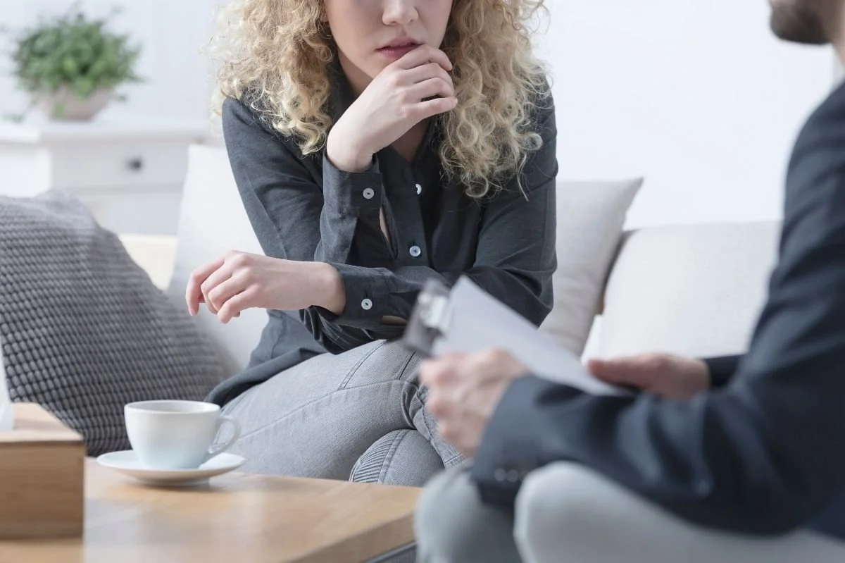 Woman sitting thoughtfully while speaking with therapist who is holding a clipboard during counseling session.