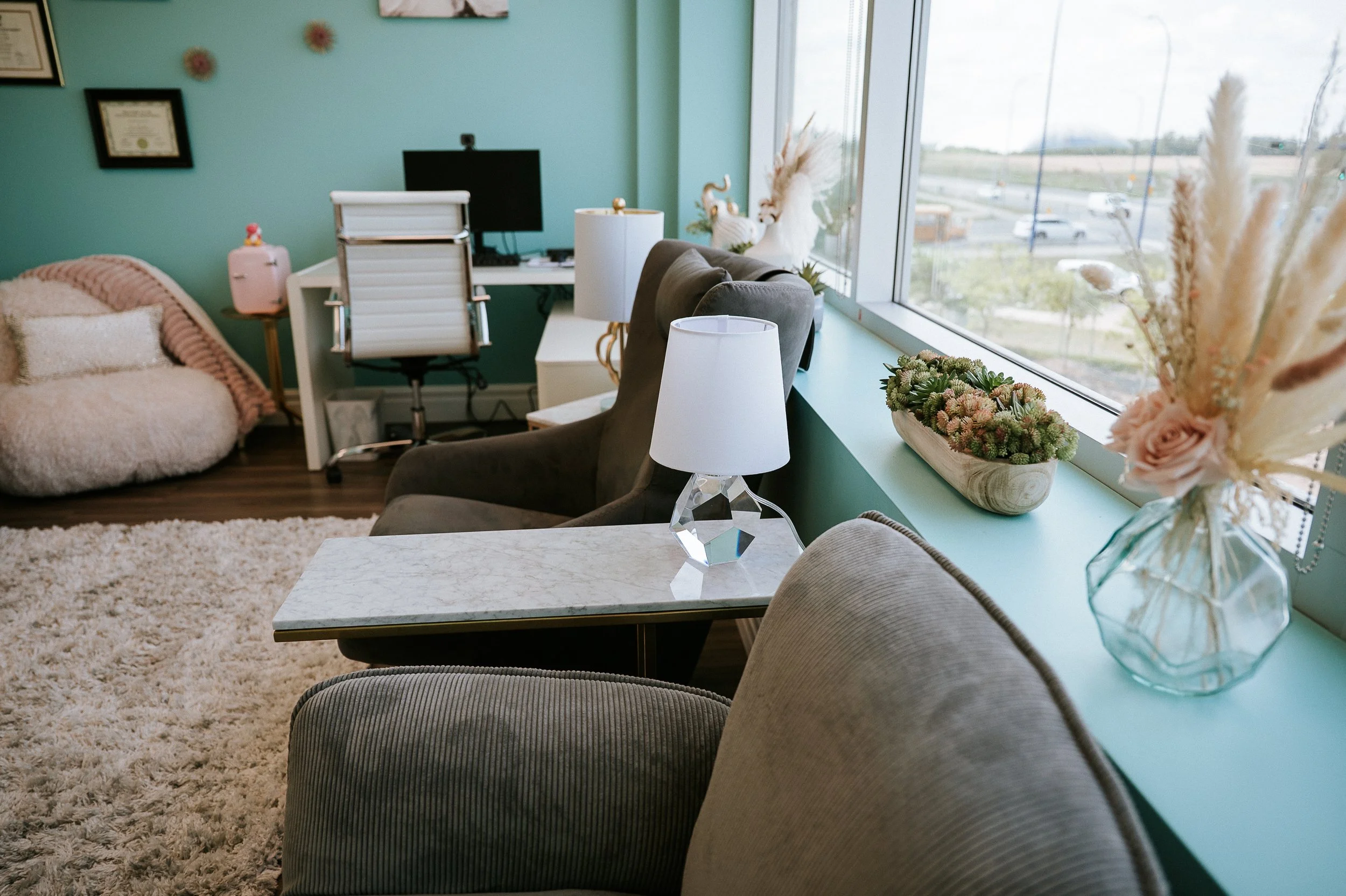 Comfortable counseling office interior with armchairs, desk workspace, soft lighting and large window.