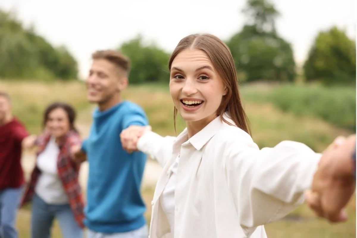 Young adults holding hands in a circle outdoors during a peer support or group therapy activity.
