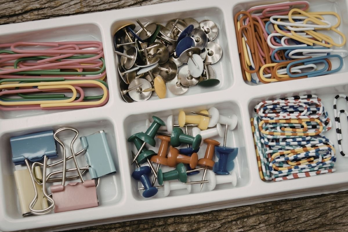 Organized desk supplies including paper clips, binder clips, push pins, and rubber bands arranged in a compartment tray.
