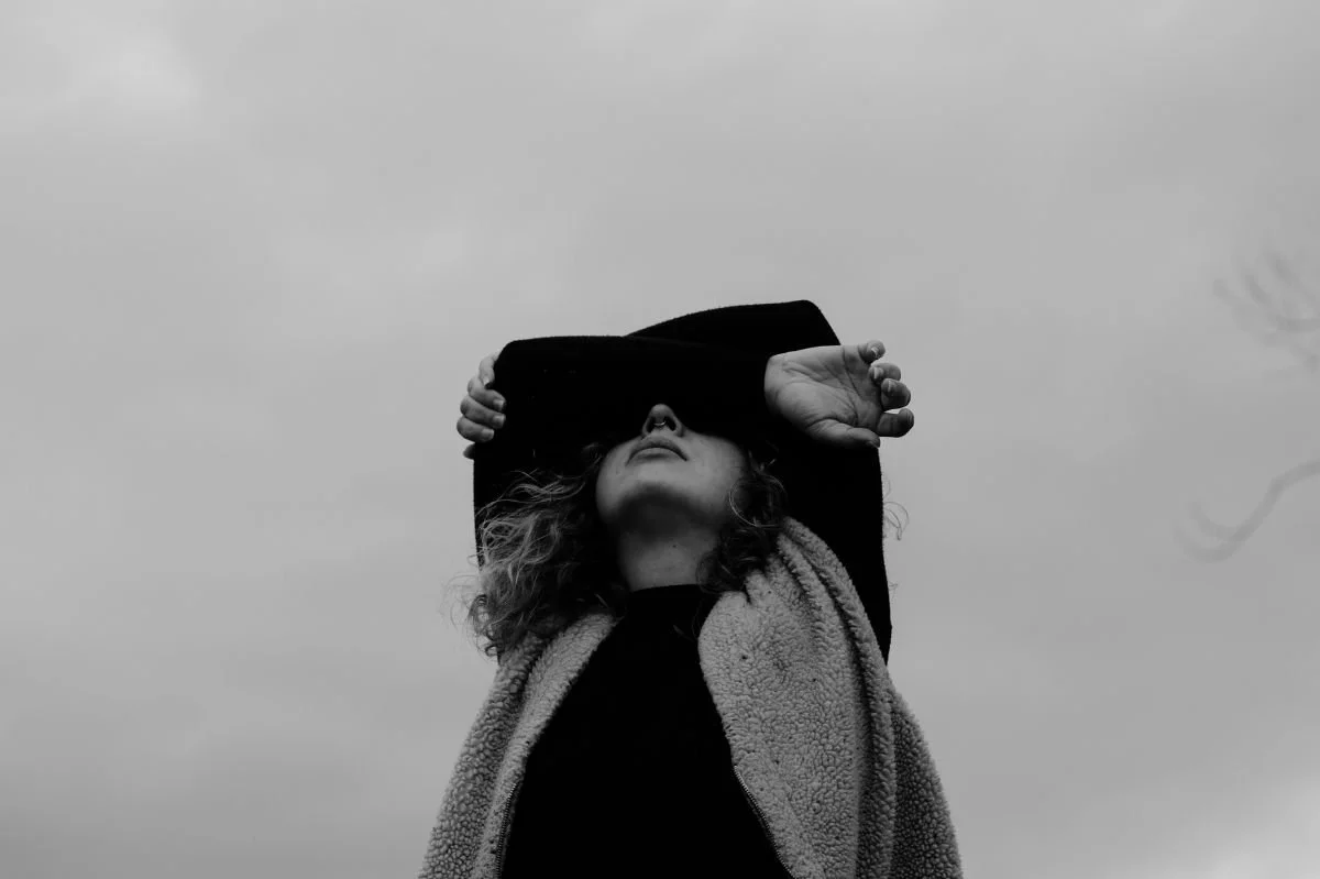 Black and white image of woman covering her face with her arms, expressing emotional distress or overwhelm.
