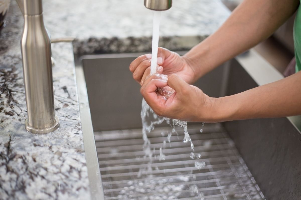Person washing hands under running water in a kitchen sink.