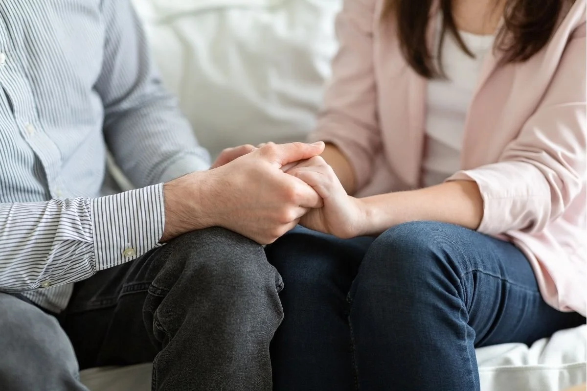 Close up of couple holding hands while sitting together during a relationship counseling session.