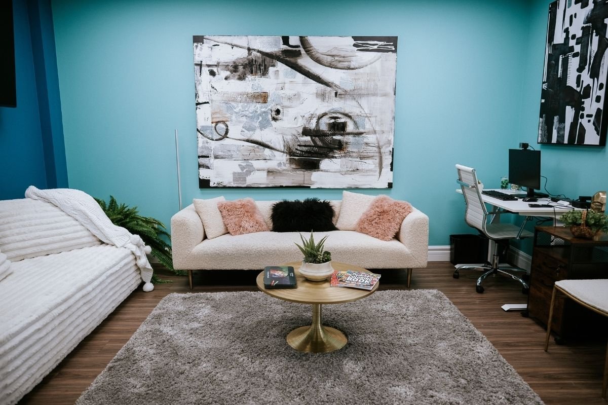 Modern counseling office with cream sofa, abstract artwork, teal walls, and desk workspace.