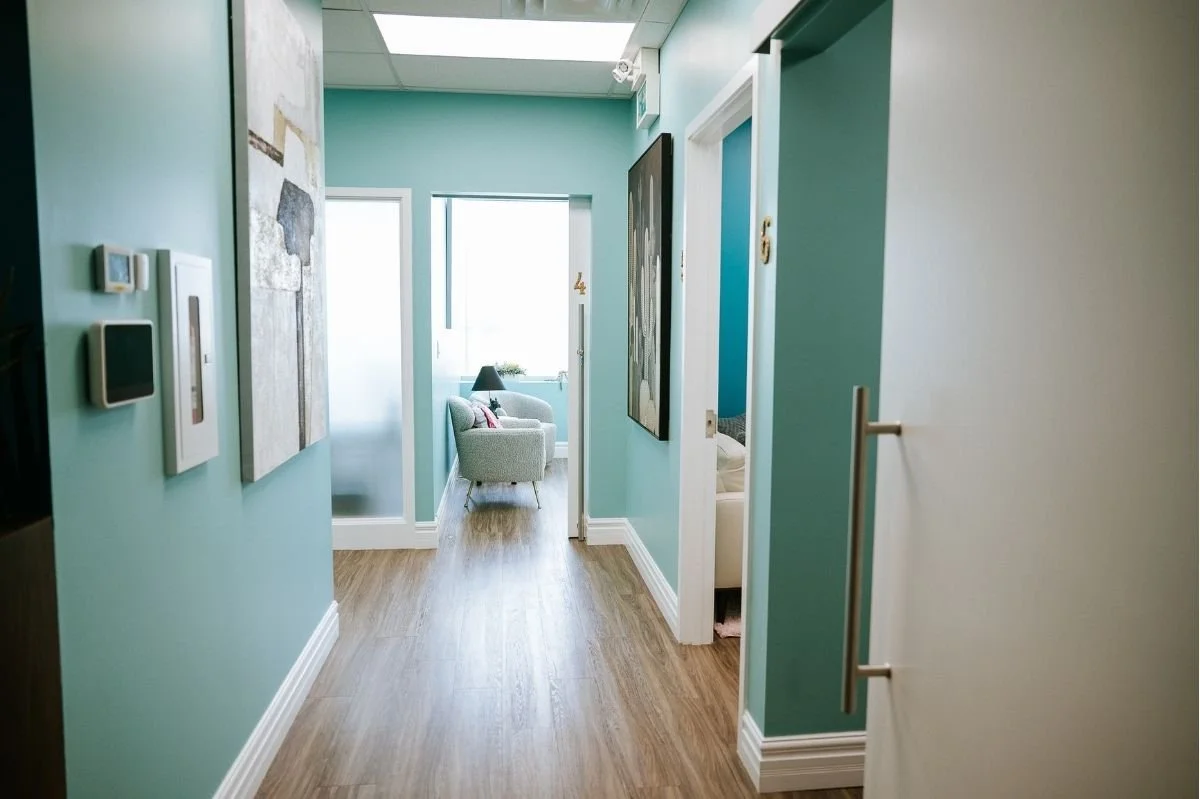 Bright hallway inside a therapy clinic with teal walls, wood flooring, and office rooms.