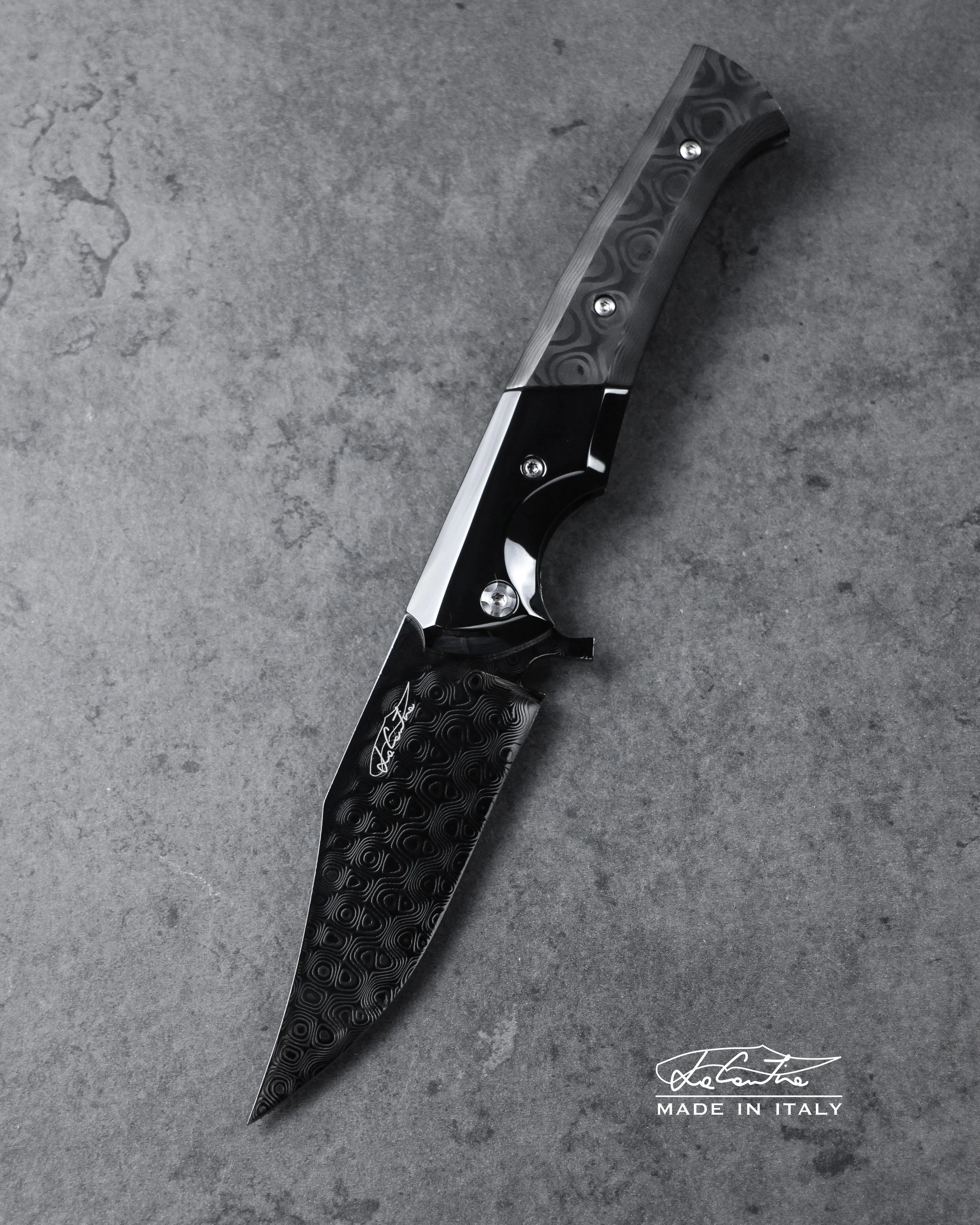 LAMA: Damasteel Rose con trattamento DLC. MANICO: Bolster, clip e meccanica in acciaio temperato con DLC, Carbonio Uniti by Fatcarbon, G10 nero, distanziale in carbonio