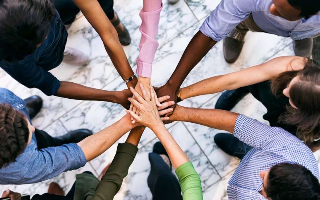 Group of diverse people placing their hands together in a teamwork gesture, seen from above on a marble floor.