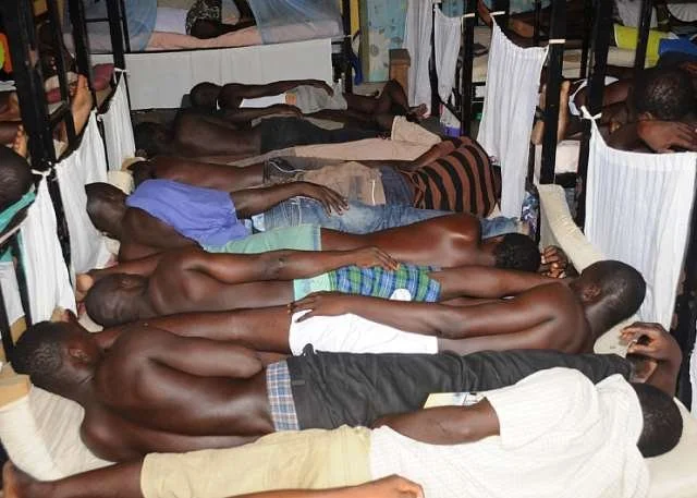 A crowded hospital ward with many men lying on beds with their heads towards the wall, appearing to be sleeping or resting.