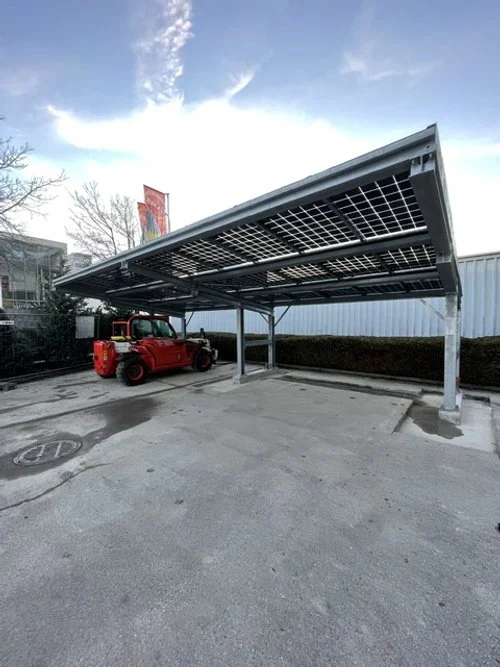 Napelemekkel felszerelt kocsibeálló vagy carport, alatta egy piros munkagéppel