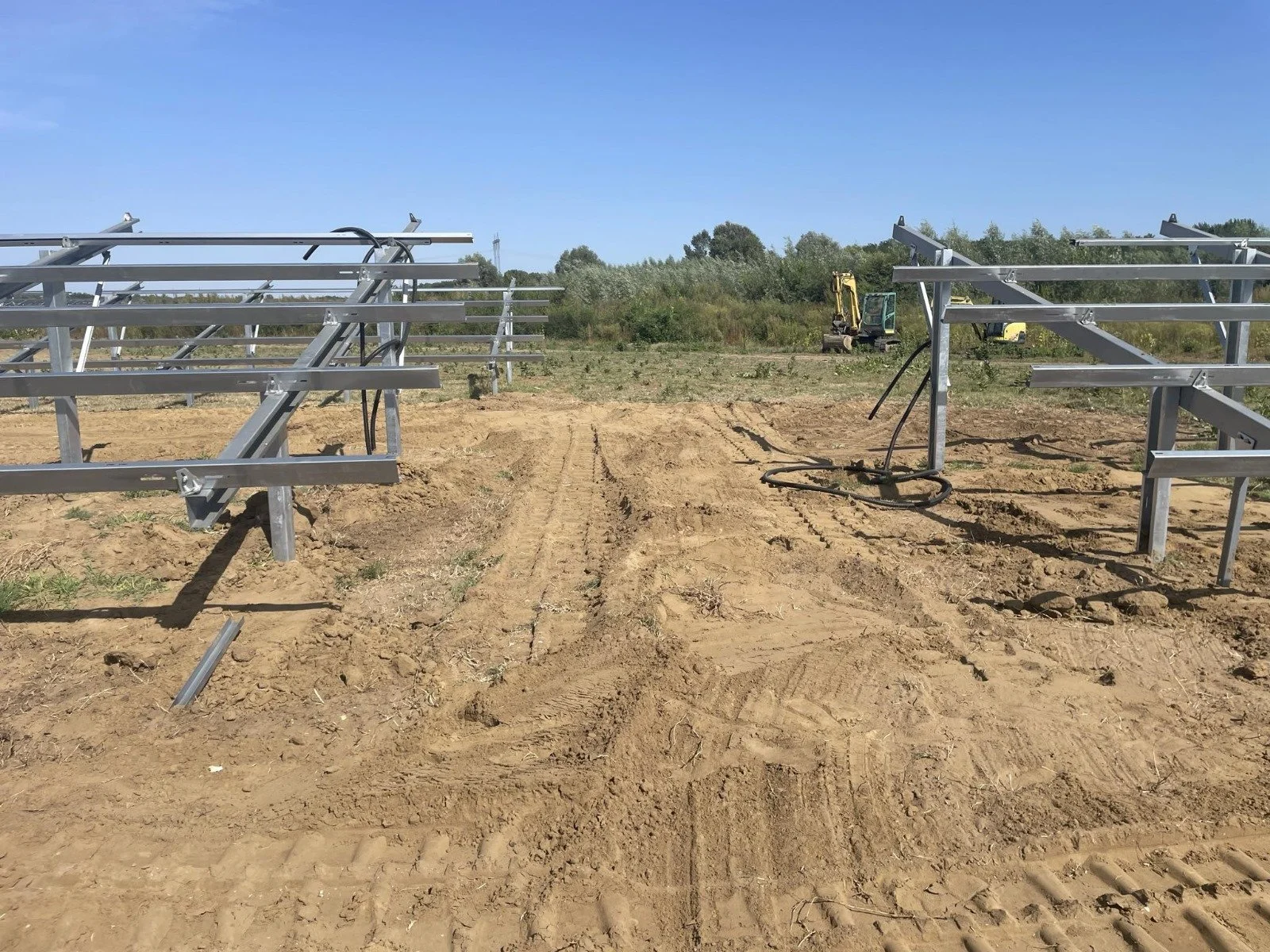 Construction site with metal framing for greenhouses on dirt ground under a clear blue sky.
