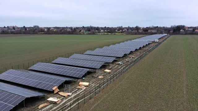 A row of solar panels installed in a field, with a fence and open grassy farmland extending into the distance.