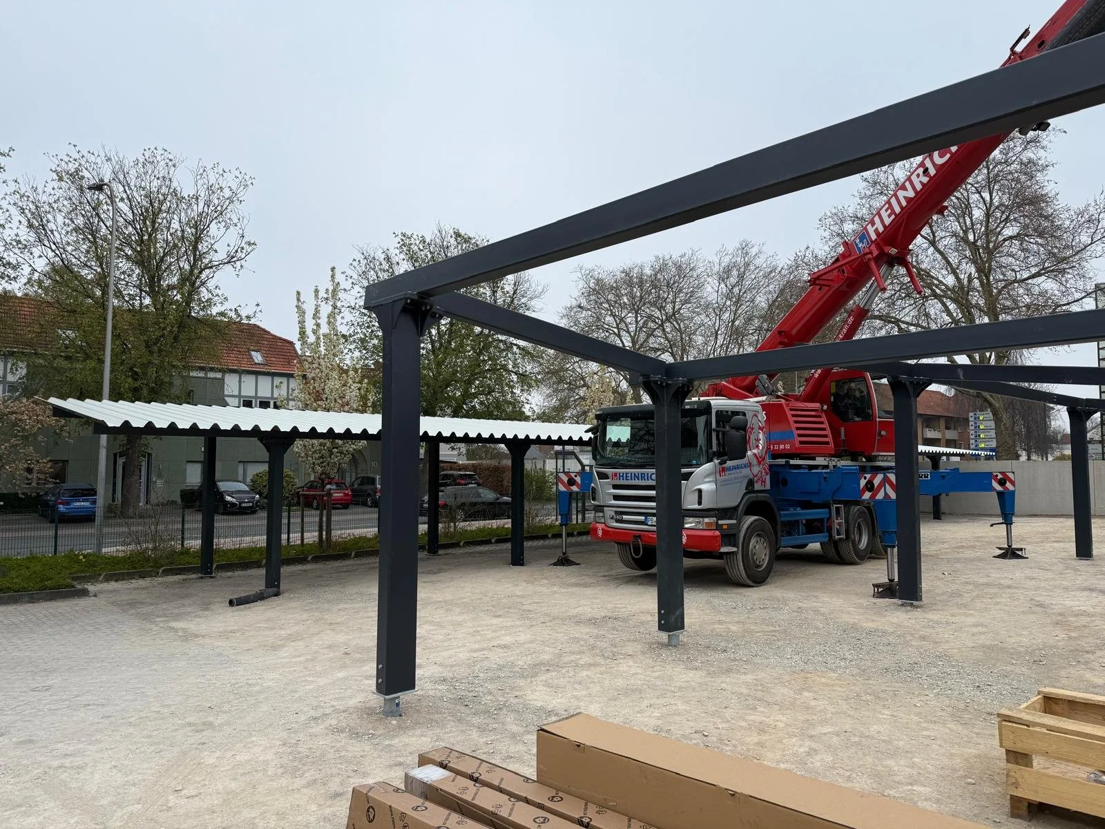 Construction site with a red crane truck and black steel framework for a building.

This is an under-construction building with steel framework, a red crane truck, and a shed with a white roof in the background.