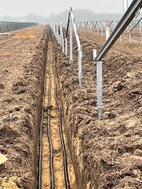 A trench in the ground with electrical wires and metal poles, likely part of a solar panel installation.