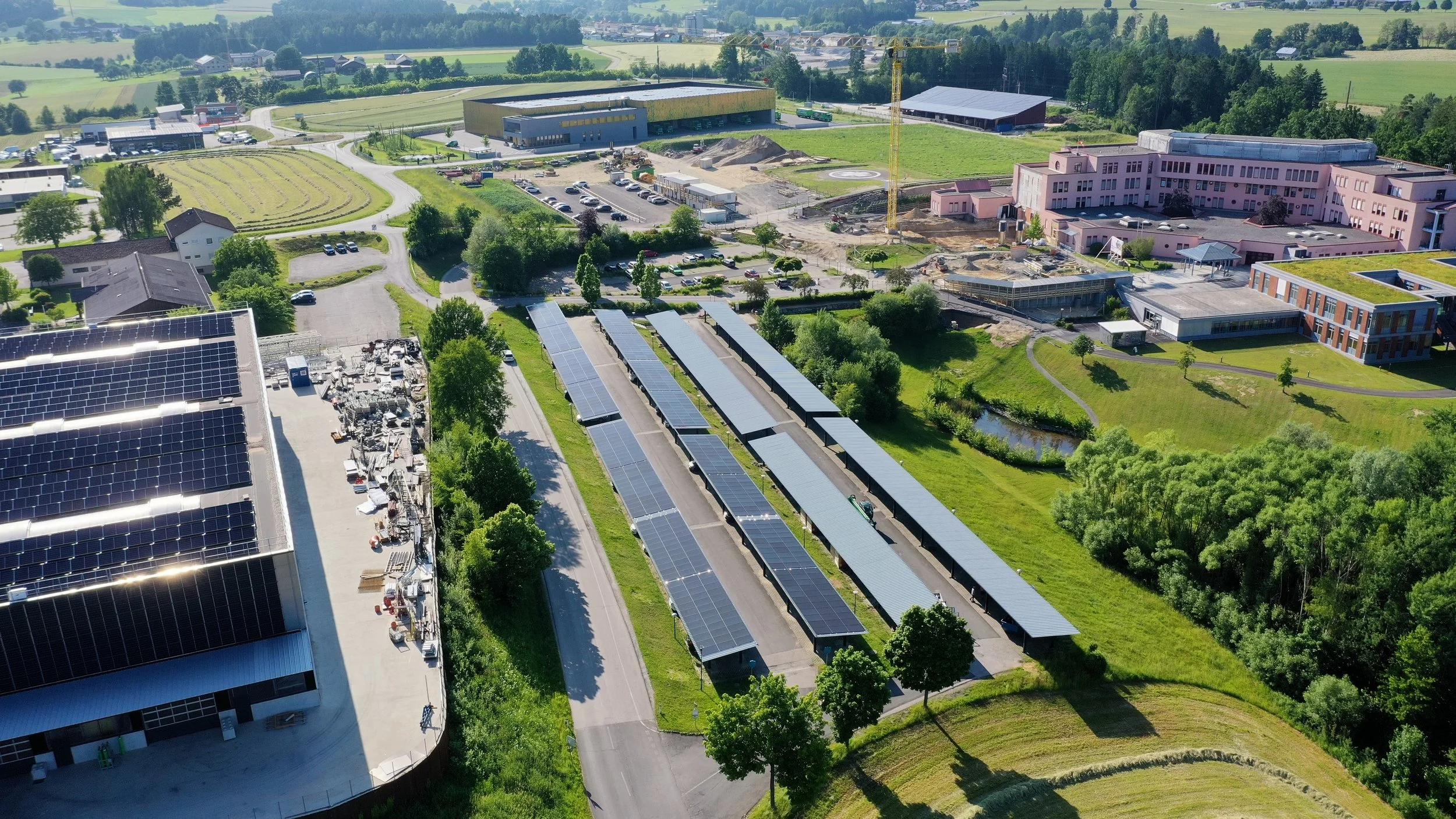 Aerial view of a facility with extensive solar panel arrays, surrounded by green fields, buildings, and trees.