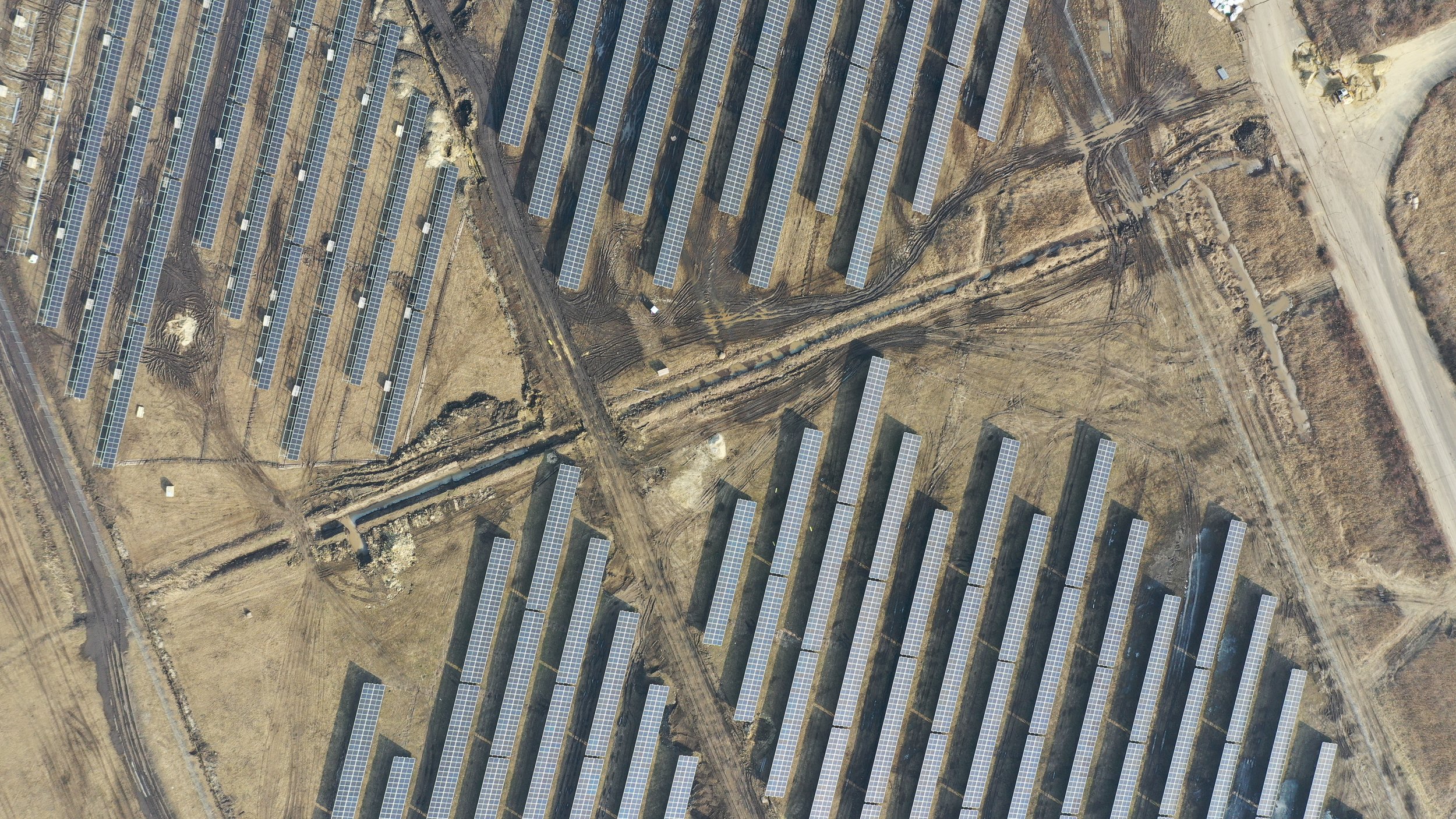 Aerial view of a solar farm with multiple rows of solar panels on a dry, brown landscape with dirt roads.