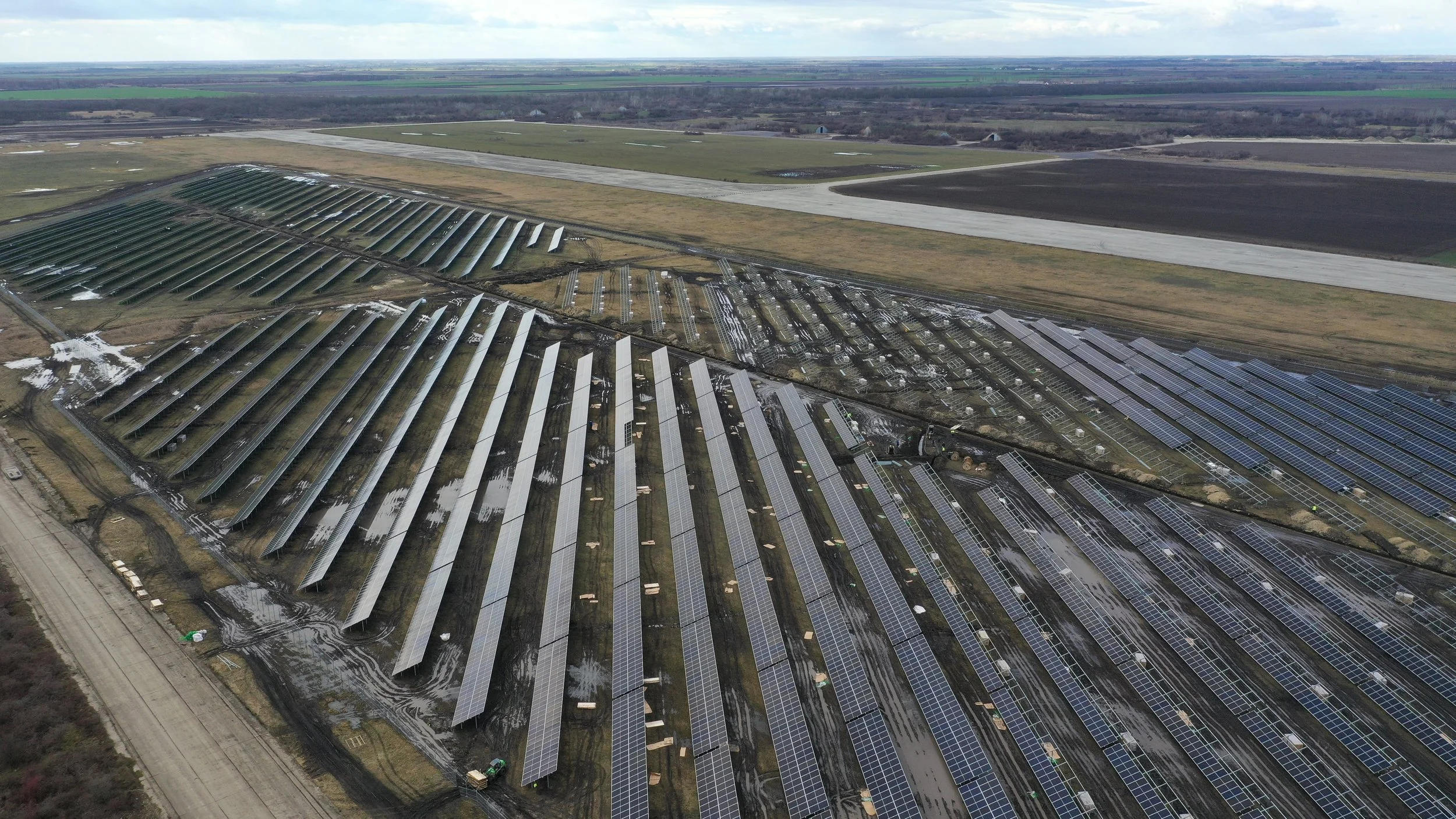 Aerial view of a solar farm with rows of solar panels on a partly cloudy day.