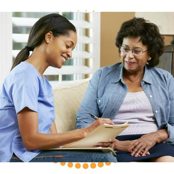 Nursing assistant taking notes while speaking with an elderly woman at home.