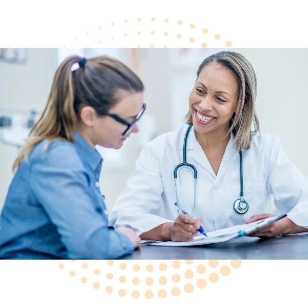 A female doctor smiling and talking with a young female patient in a medical office.