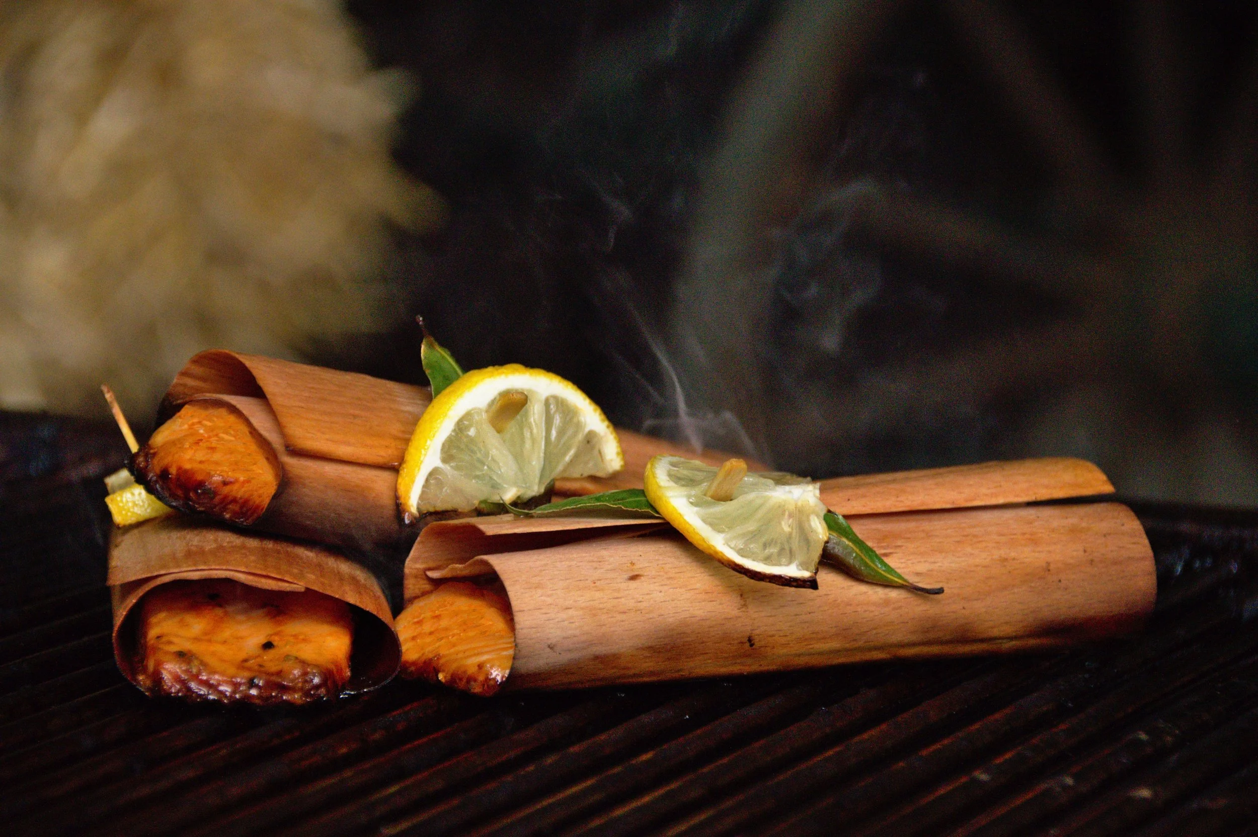 Gegrillte Süßkartoffeln, garniert mit Zitronenscheiben und Basilikumblättern, auf einem Grillrost, Rauch steigt auf.