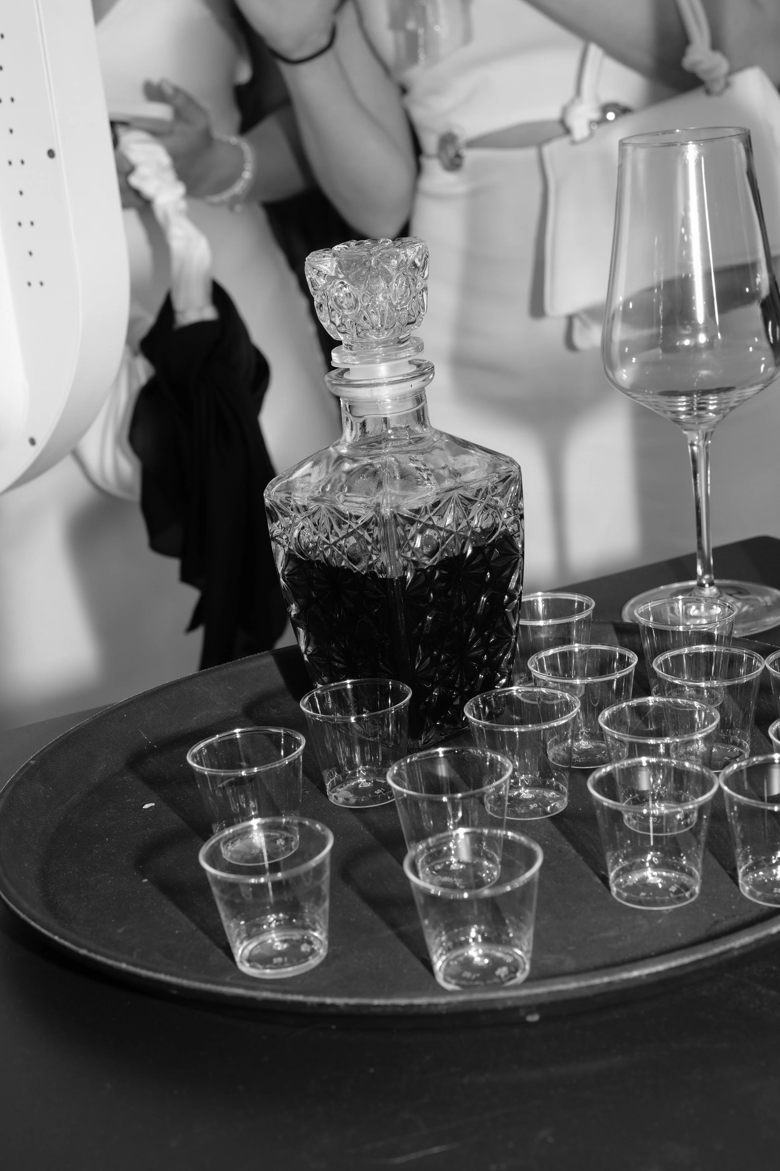 Eine Karaffe mit dunklem Likör oder Wein, umgeben von mehreren kleinen leeren Schnapsgläsern auf einem schwarzen Tablett.