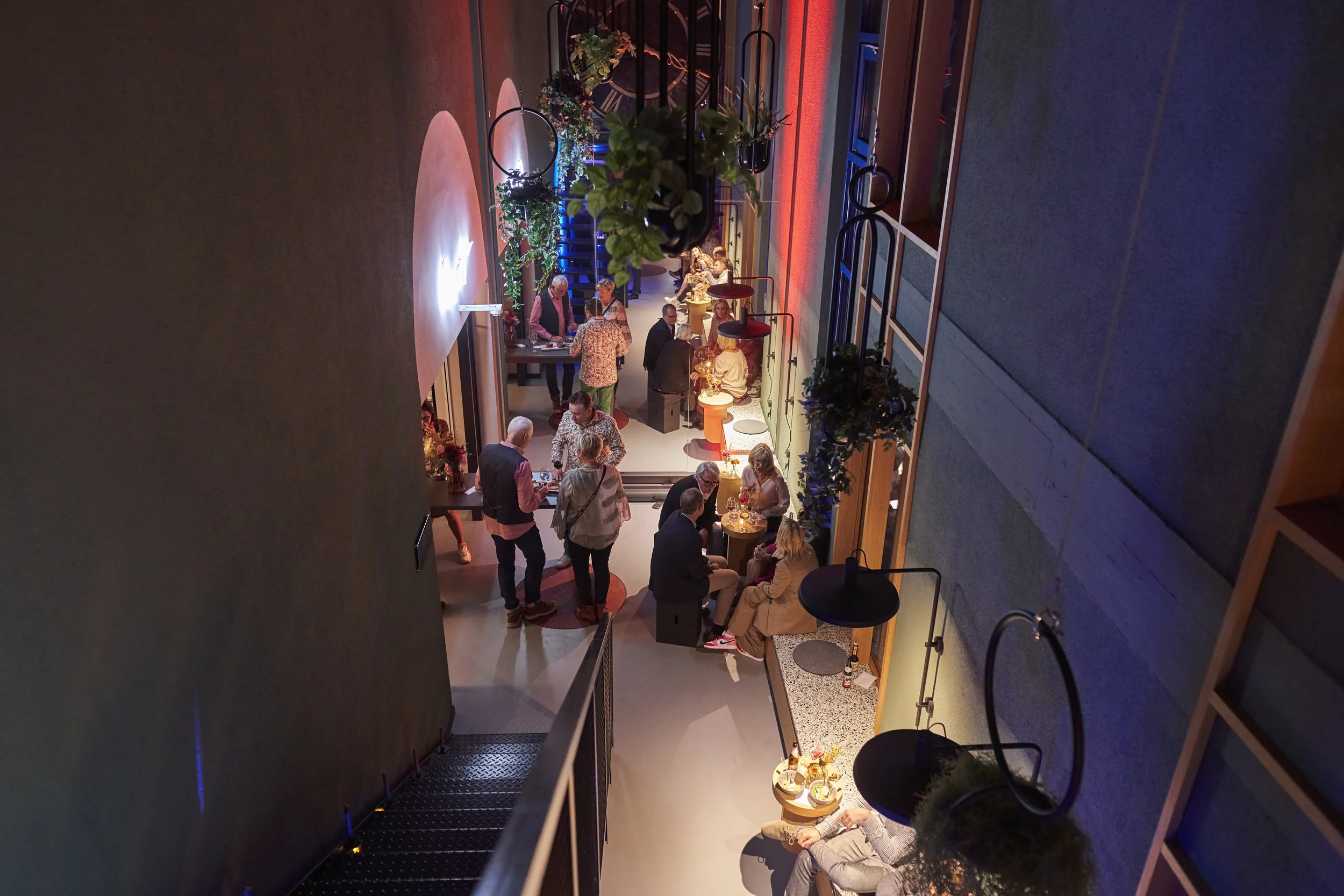 Menschen feiern ins Atrium der Urban Spaces in einer modern gestalteten, mehrstöckigen Bar oder Lounge mit warmer Beleuchtung, Pflanzen und dekorativen Lichtern.