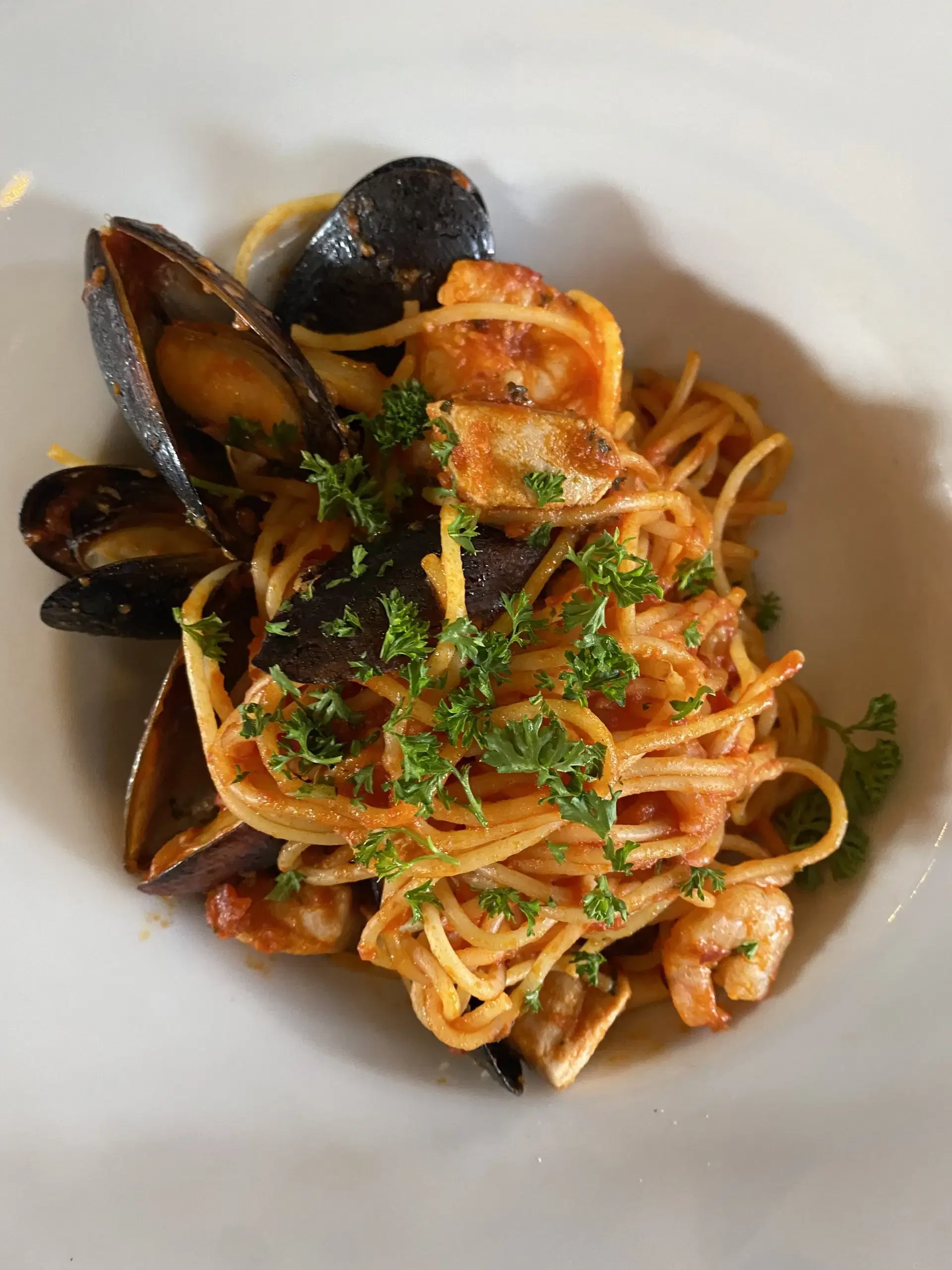 A plate of seafood spaghetti garnished with parsley, featuring mussels, shrimp, and a tomato-based sauce.