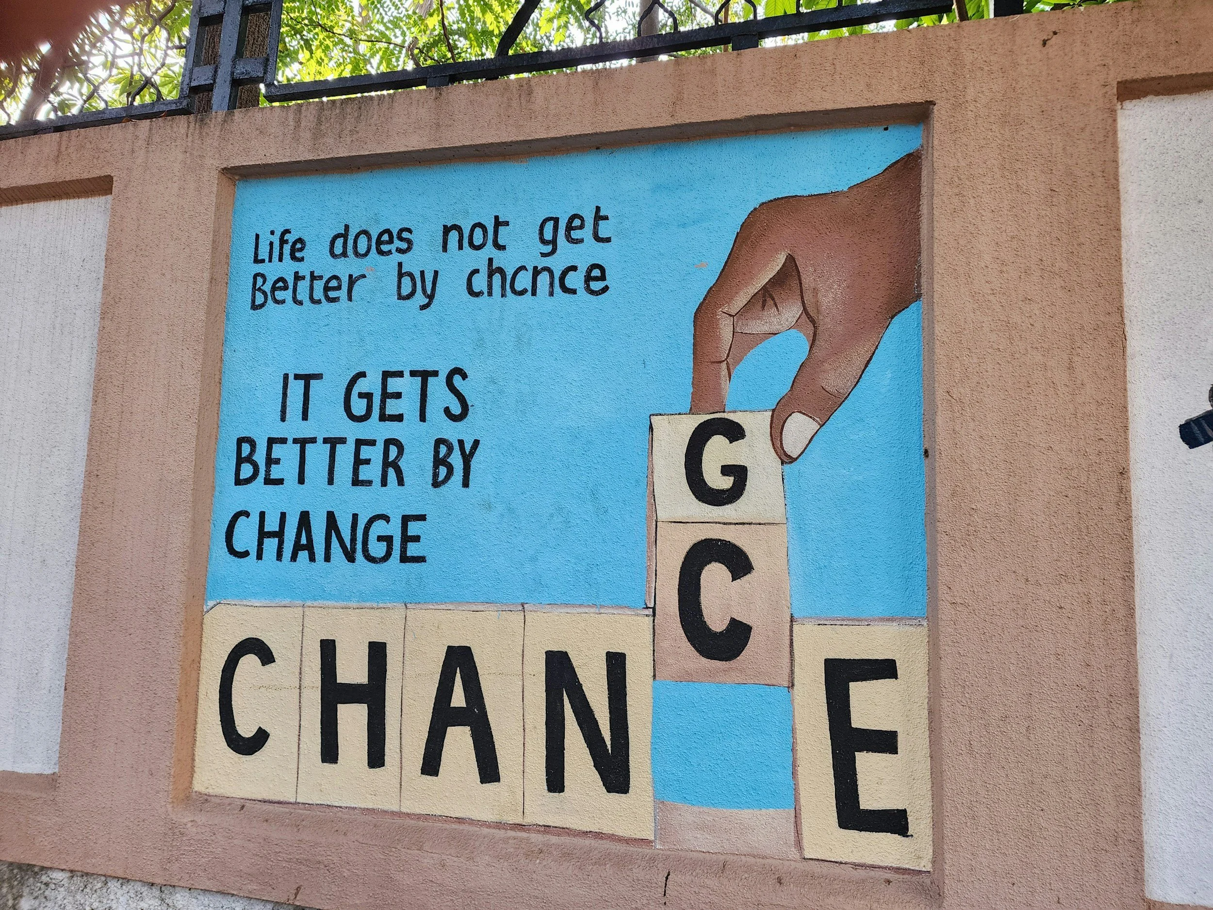 Painted wall with a hand stacking letter blocks spelling coach and the message, "Life does not get better by chance, it gets better by change."
