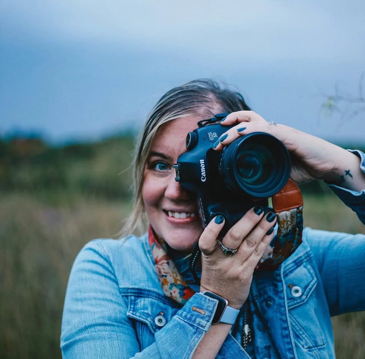 A woman with blue eyes taking a photo with a Canon camera outside in a field