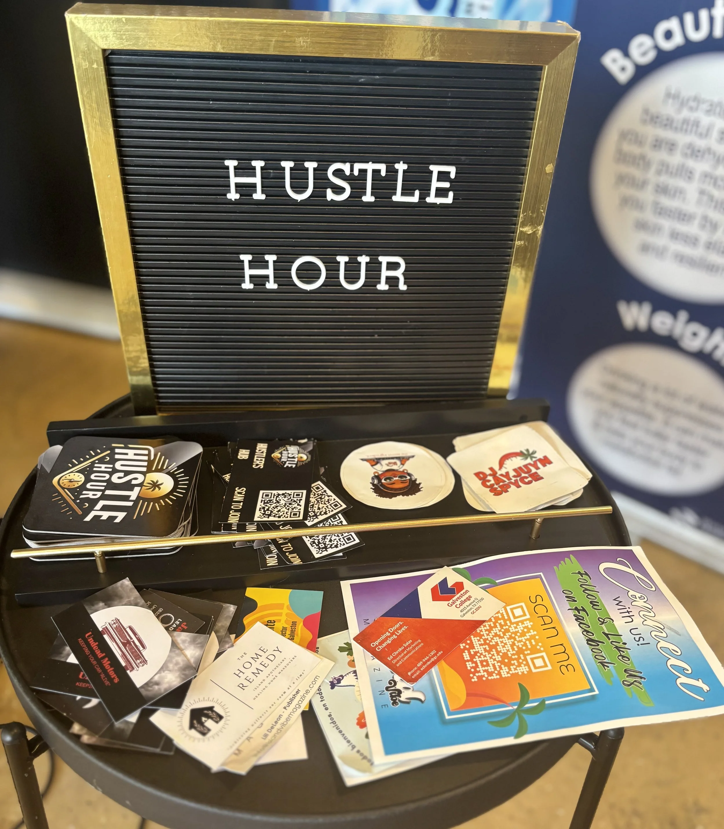 Table with promotional items and flyers, a letter board with white letters spelling 'HUSTLE HOUR'.