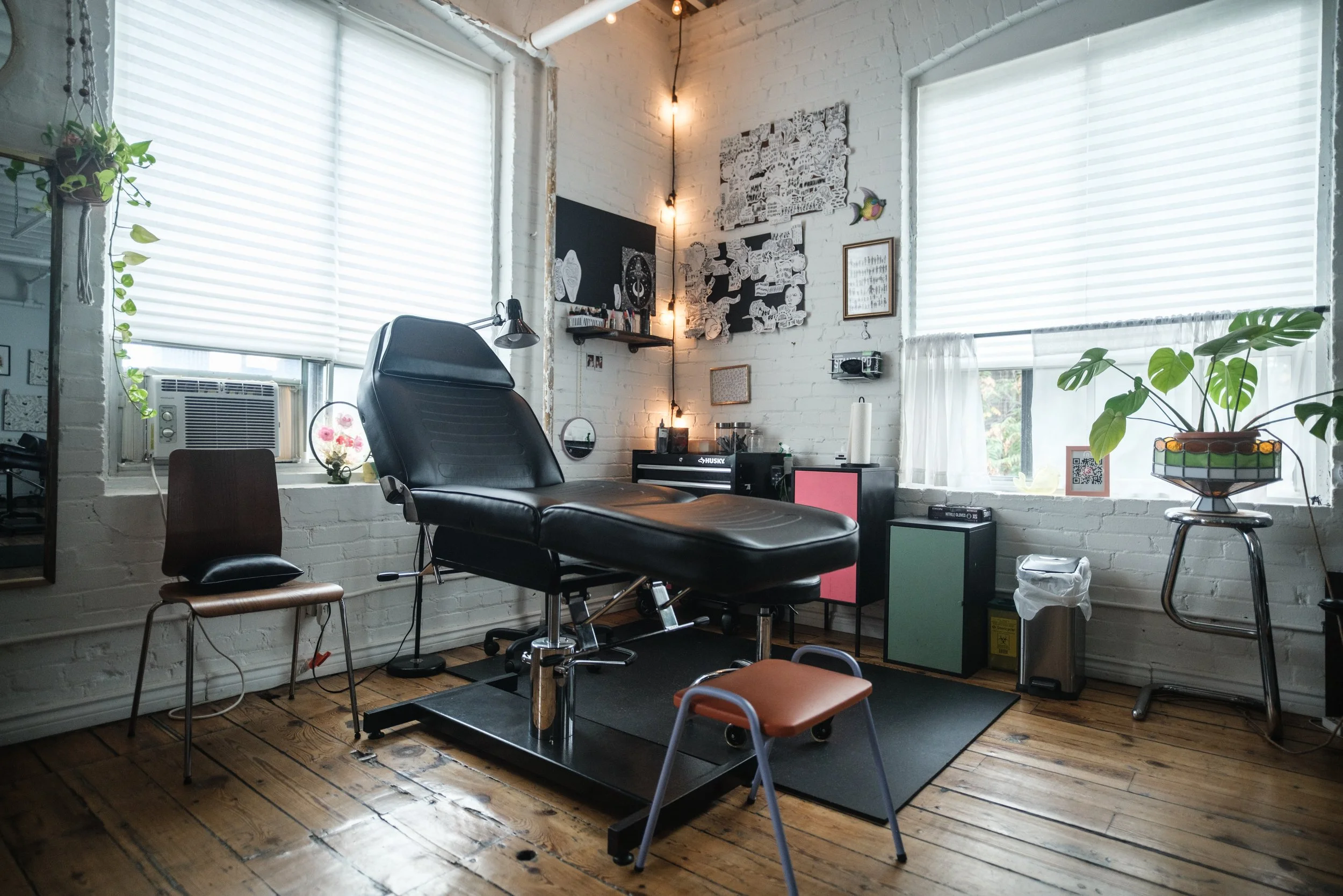 A reclining tattoo bed at a station . Printed flash designs adorn the walls and string lights provide a warm ambience.