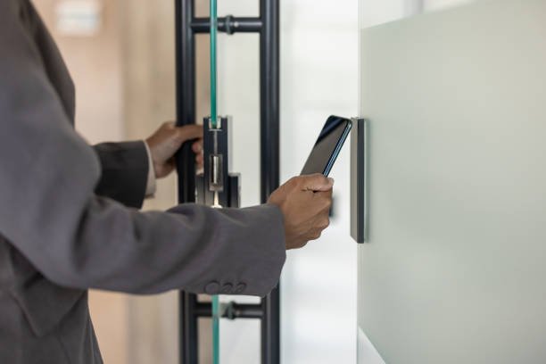 Person in a suit using a smartphone to scan or interact with a security or access control device on a wall.