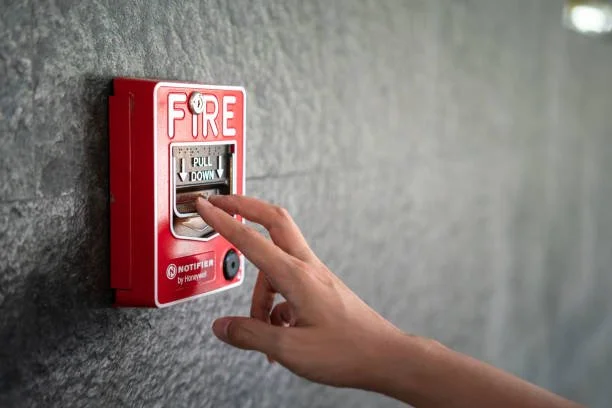 A person pulls down a fire alarm pull lever mounted on a gray concrete wall.