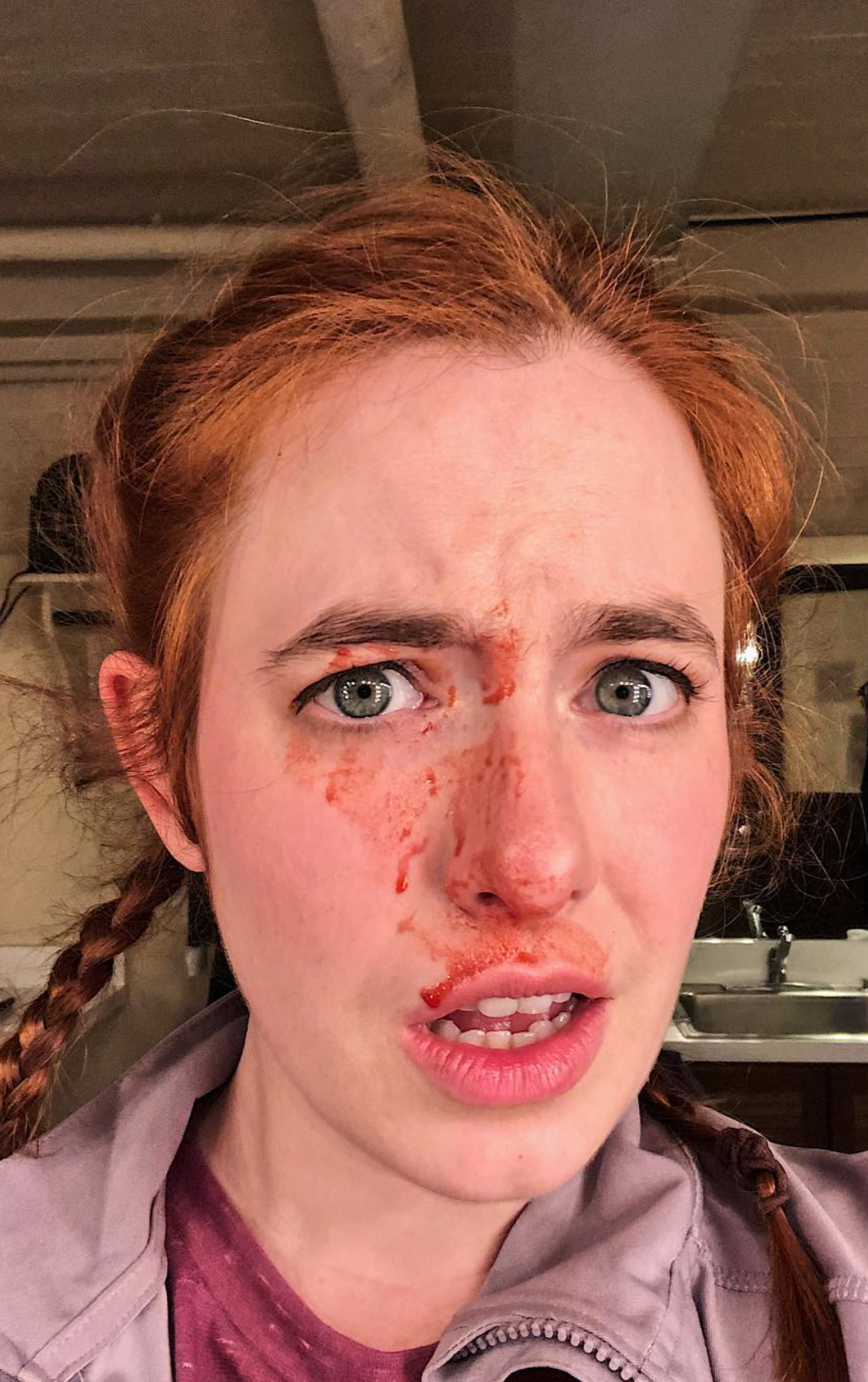 A woman with red hair and braids with theatrical fake blood on her face.