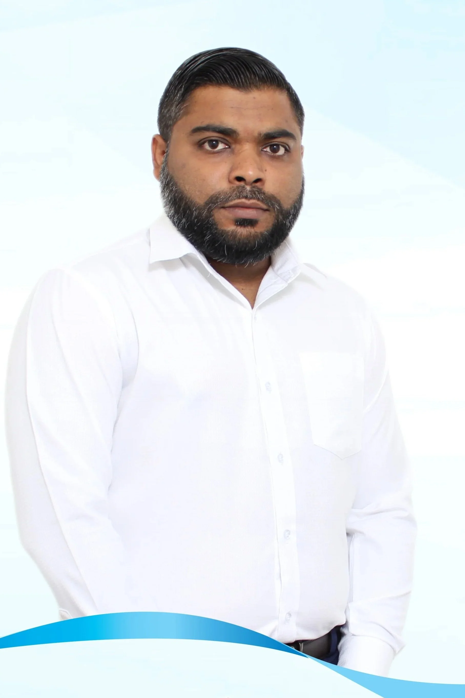 Portrait of a man with a beard and short, neatly styled hair, wearing a white shirt, in an indoor setting with blurred background.