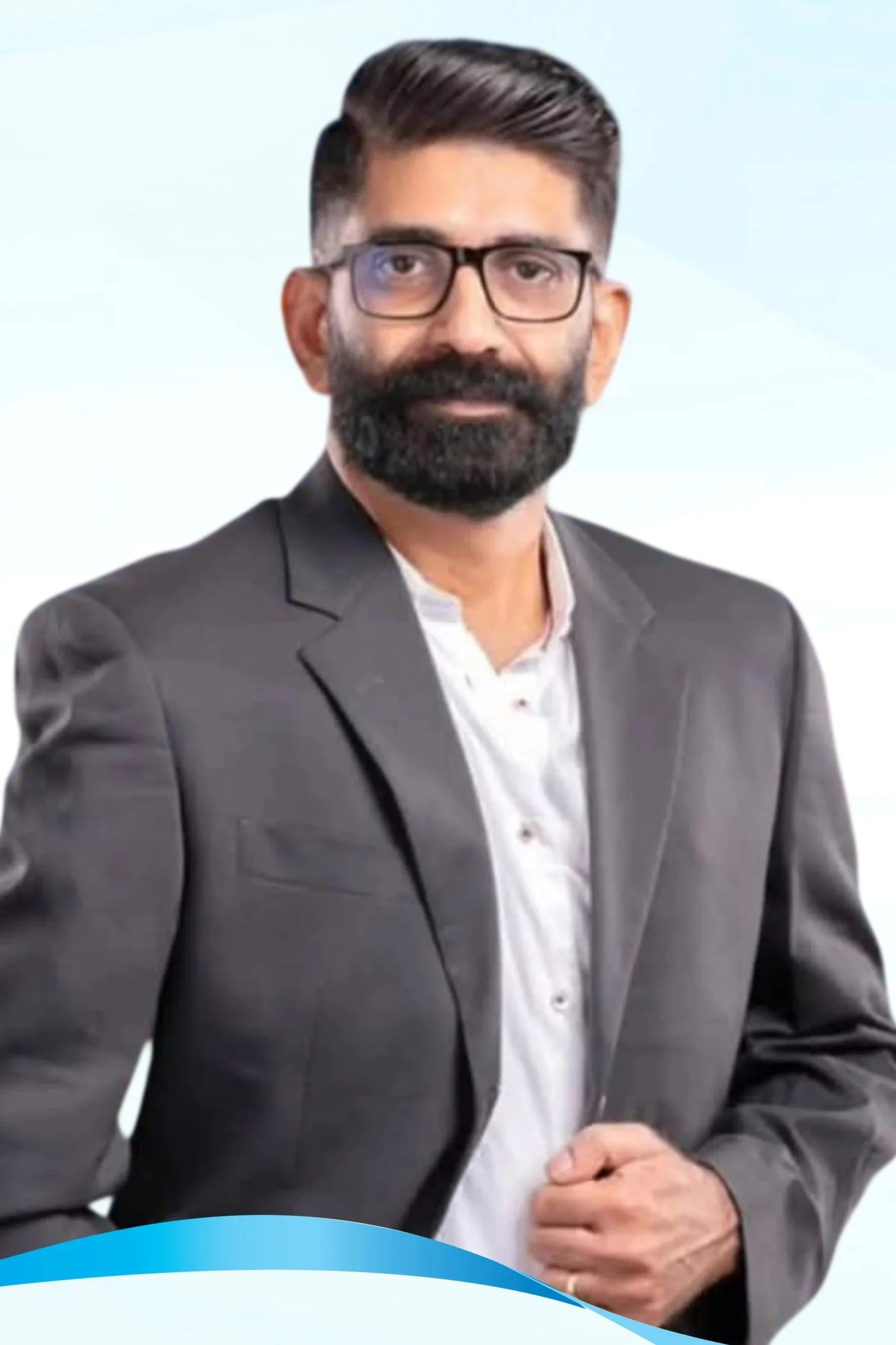 Professional man with glasses and a beard wearing a gray suit and white shirt, posing indoors with blurred background.