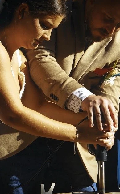 man and woman at wedding, smiling, pressing on an iron, branding their name onto wood on a sunny day.