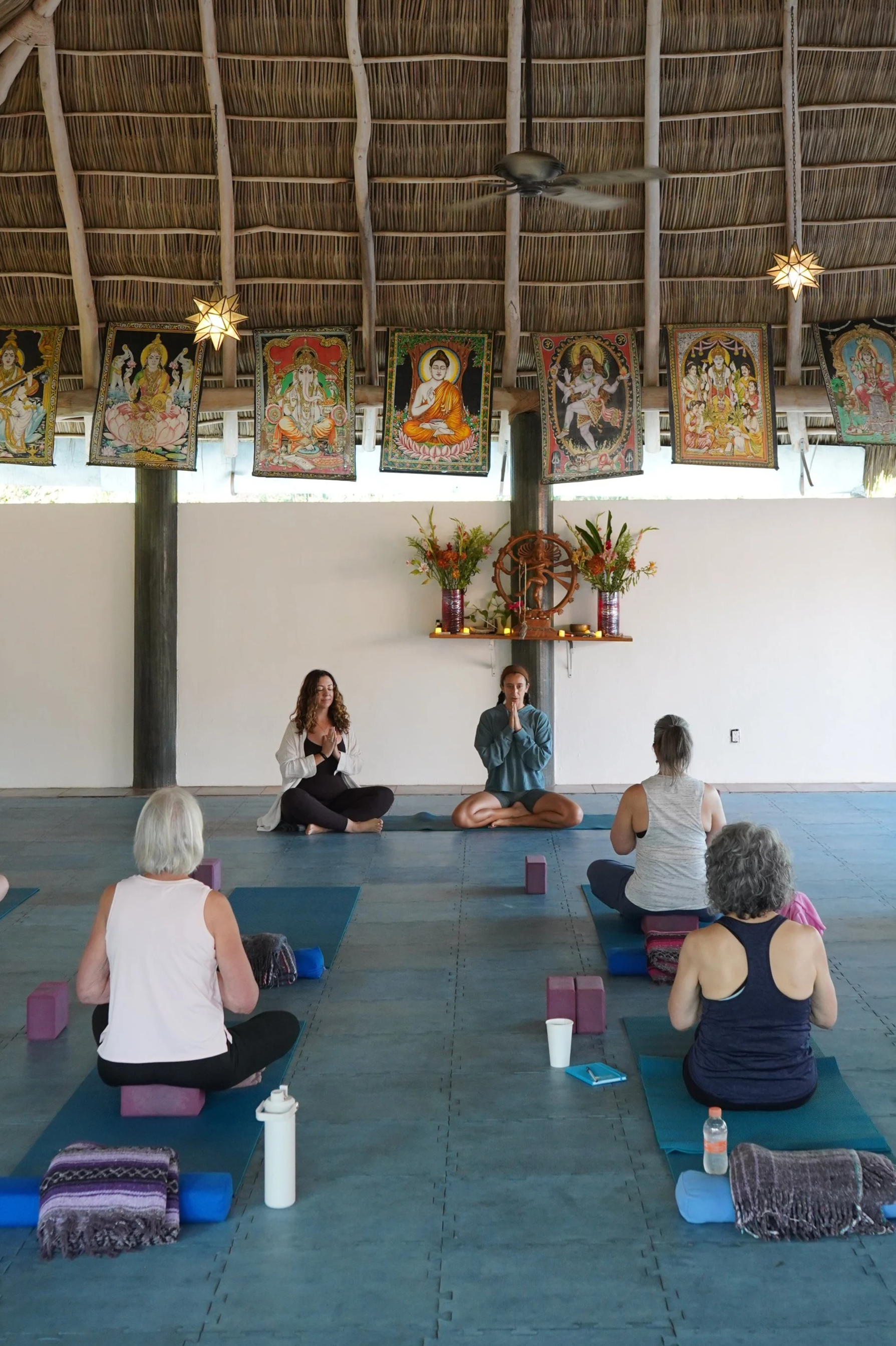 Group meditation and gentle yoga practice during a Sol Collective retreat in Sayulita, Mexico, inside an open-air yoga shala with traditional artwork and tropical architecture