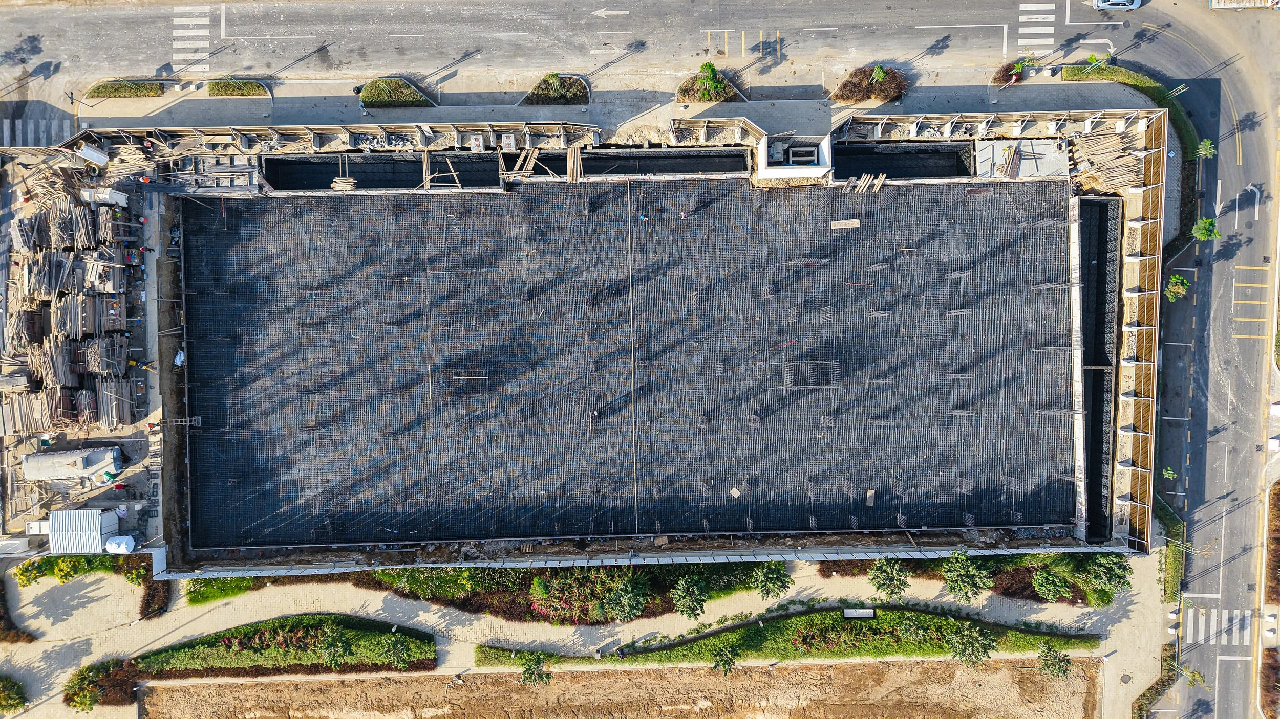 A family of three stands outside a modern building with white and brown exterior, with a black car driving by in the foreground. The image has an overlay with the text 'Coming Soon' and Arabic writing.