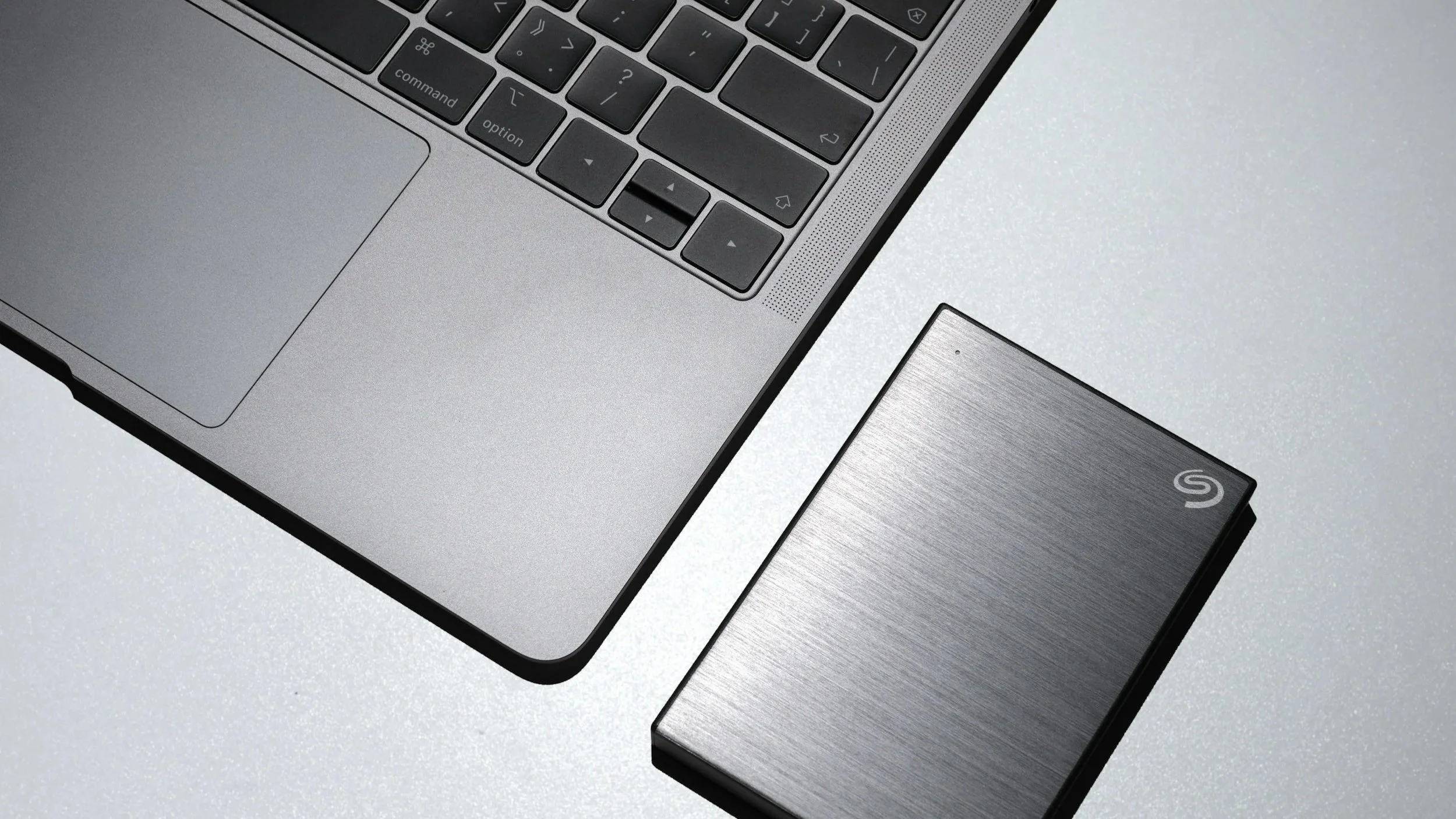 Une surface en métal gris clair avec un ordinateur portable en haut à gauche et un disque dur externe en dessous à droite.