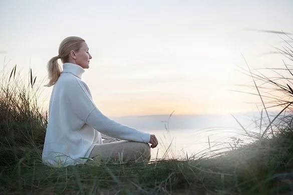 Woman gently holding her chest while standing outdoors, representing somatic grounding and nervous system safety during extended coaching sessions.