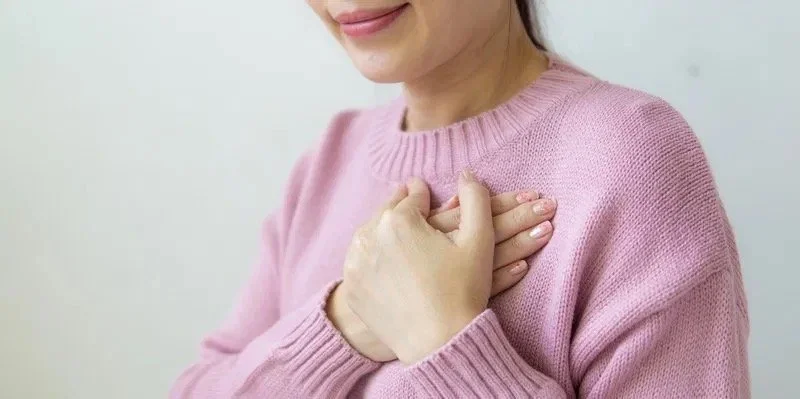 A woman gently resting her hands on her chest in a self-soothing gesture, symbolizing somatic grief healing and nervous system regulation.